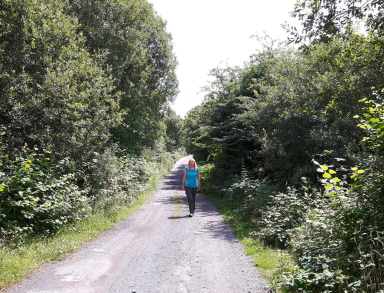 A woman walking along a gravelled path in woodland.