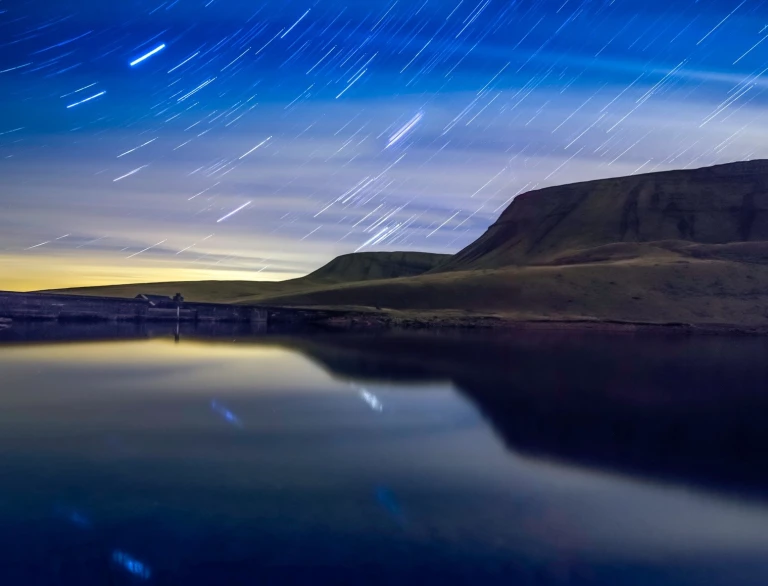 An evening photo of a lake and mountains with a starry sky in the background.