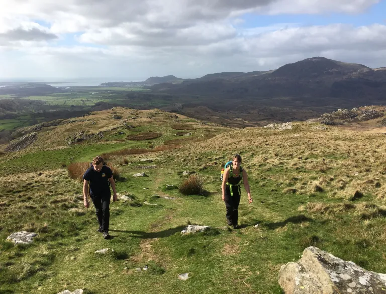 Walking on a high path with mountains and coast in the background.