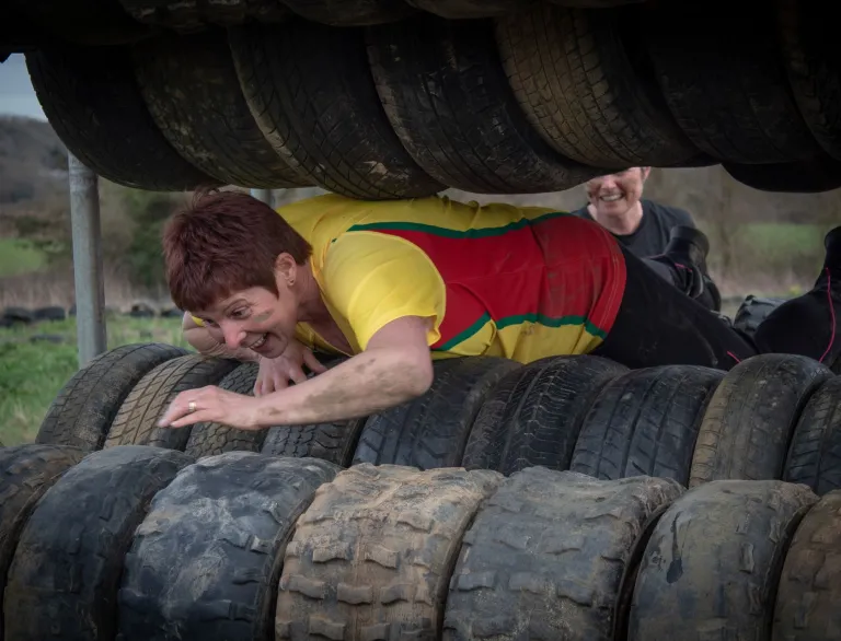 A woman climbing through tyres on a muddy course