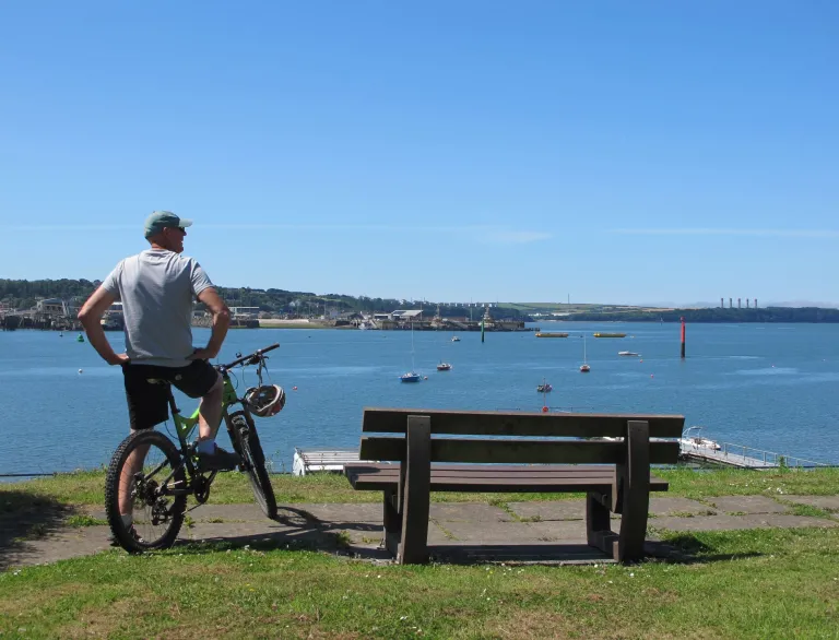 cyclist on bike next to bench looking at marina on a sunny day.