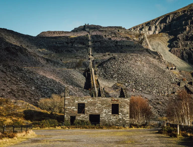 Überreste eines Schiefersteinbruchs mit einem Hang voll Schieferabraum und alten Gebäuden.