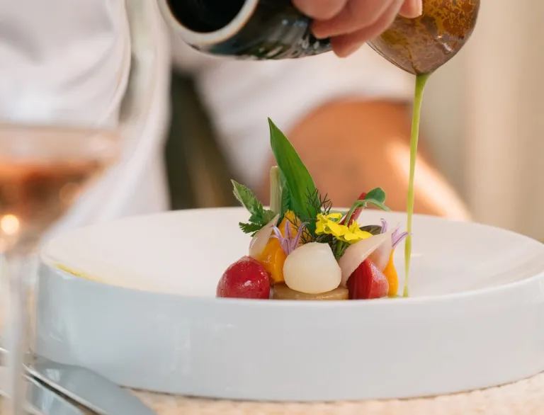 A small plate of food being drizzled with dressing at a restaurant.