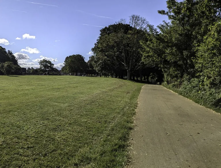 A wide shared cycle/walking path next to a large field/park.