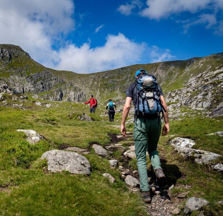 Climbers walking on a path towards a rocky mountain flecked with green.
