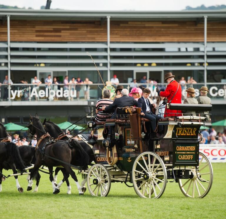 A cart being pulled by horses in a show arena at an agricultural festival.