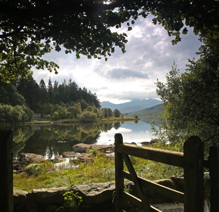 A scene of the lake from a gate with mountains and trees reflecting in the water.