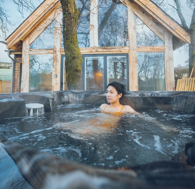 Woman relaxes in a hot tub outside a luxury treehouse.