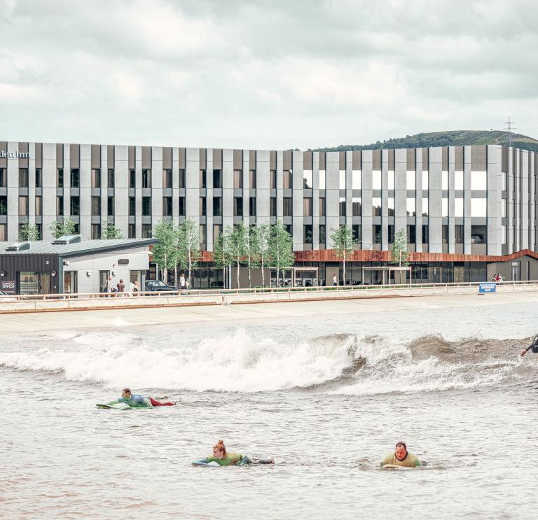 Surfers riding the waves in front of a large hotel.