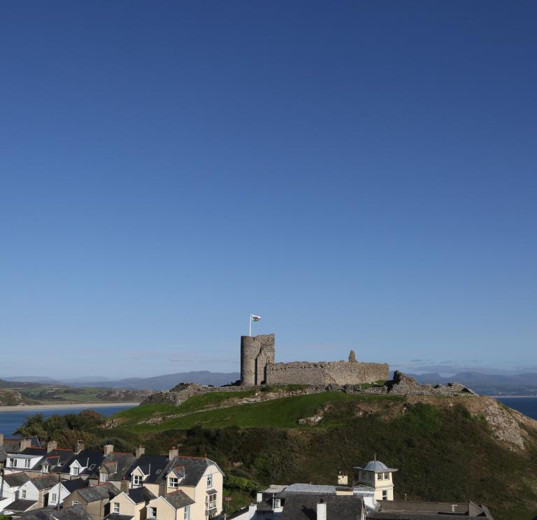 Criccieth Castle on top of a hill from afar, with the sea in the background and houses in the foreground.