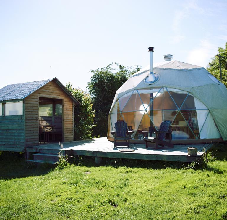  Image of a dome tent and a small hut in a field.