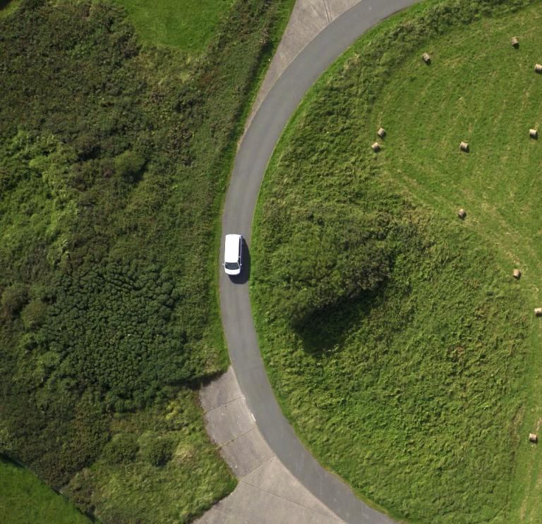 A white vehicle curving its way around a green field near Strumble Head, Pembrokeshire.