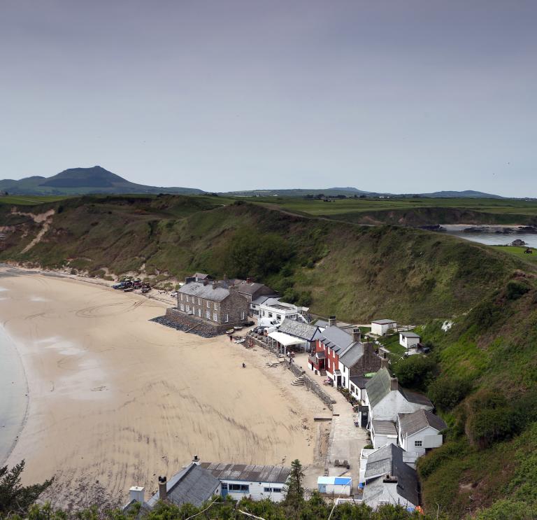 Image of buildings on the beach, backing onto green hills.