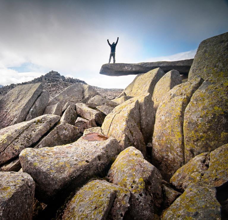 Wanderer, der die Hände in die Luft hält, auf dem Cantilever Rock, Eryri (Snowdonia)