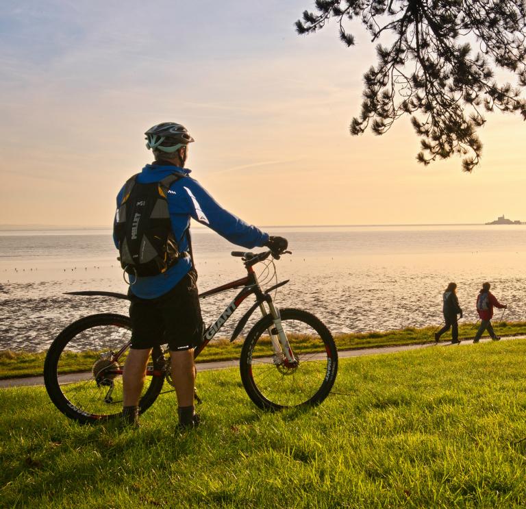 Cyclists on Coast Path at Blackpill at sunrise with Mumbles Head in background
