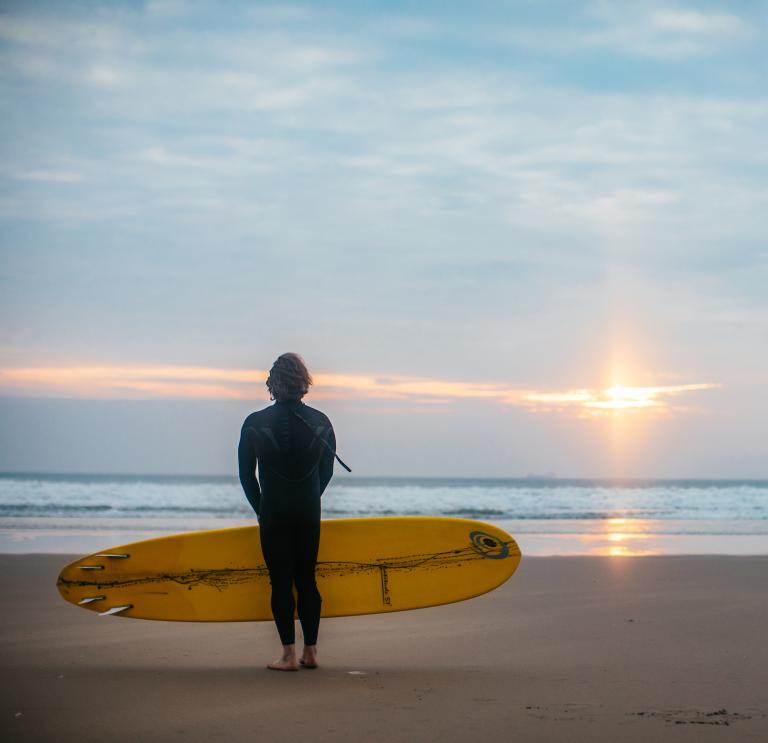 Mann am Strand von Wales mit Blick aufs Meer bei untergehender Sonne