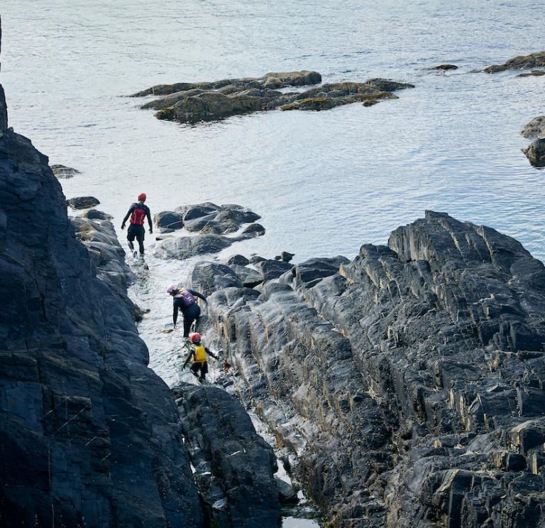 3 people climbing over rocks coasteering