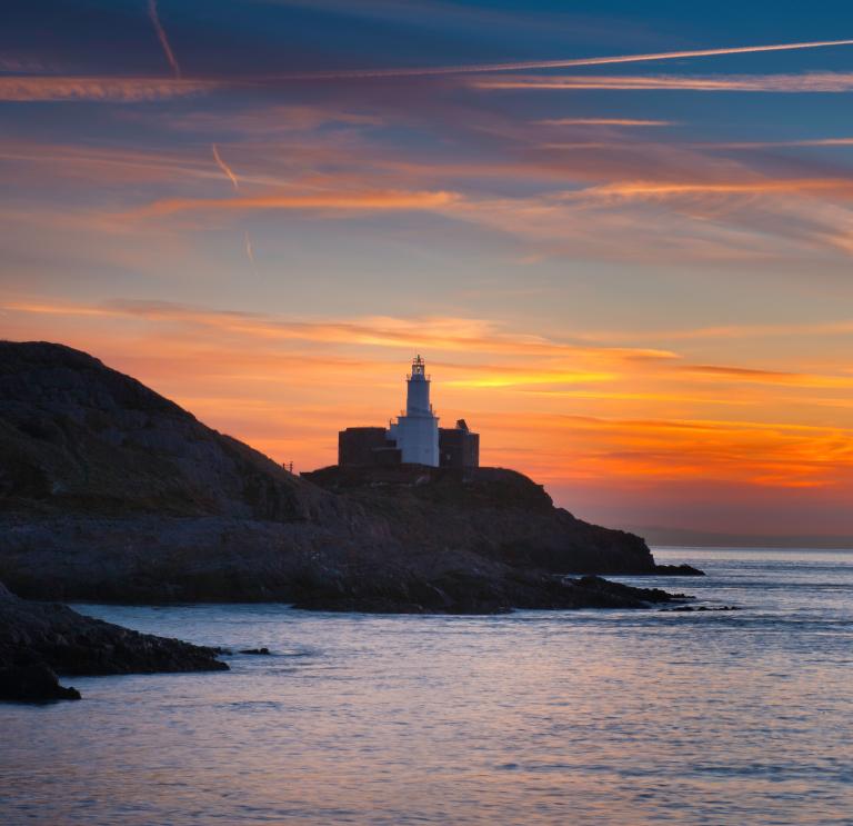 The Mumbles head lighthouse at sunrise from Bracelet Bay.