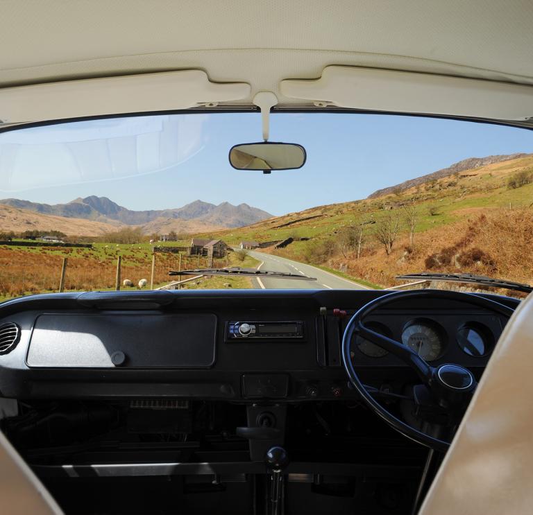 Innenansicht eines Campervans. Durch die Windschutzscheibe sieht man die Straße und die Landschaft von Snowdonia.