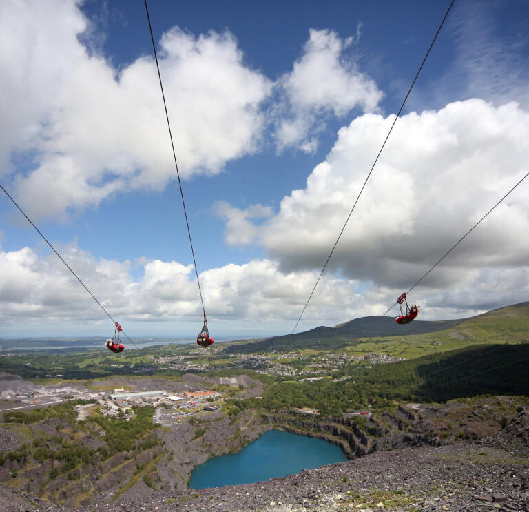 Three people on four zip lines over a deep blue lake in a quarry.