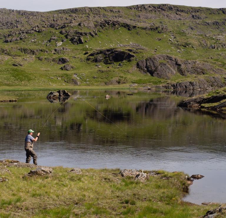 A man fishing by a lake in the mountains.