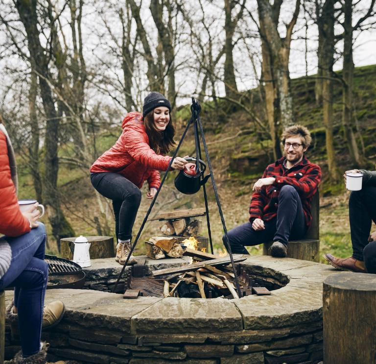 A group of people laughing round a campfire.