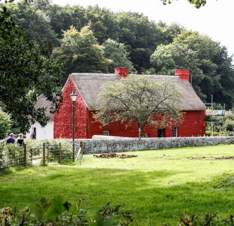 Red cottage next to a field with trees behind 