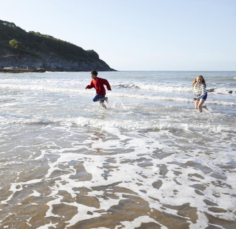 Three children running in the shallows of the sea on a beach.