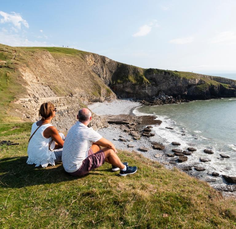 Man and woman sat on a clifftop looking out to sea.
