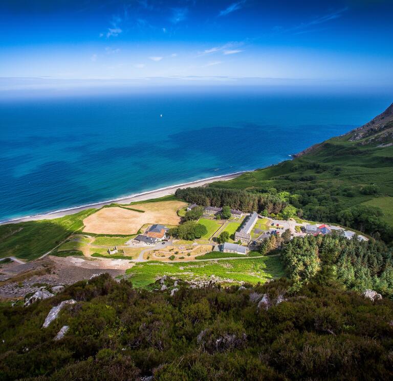 Aerial shot of Nant Gwrtheyrn surrounded by green landscape and the sea.