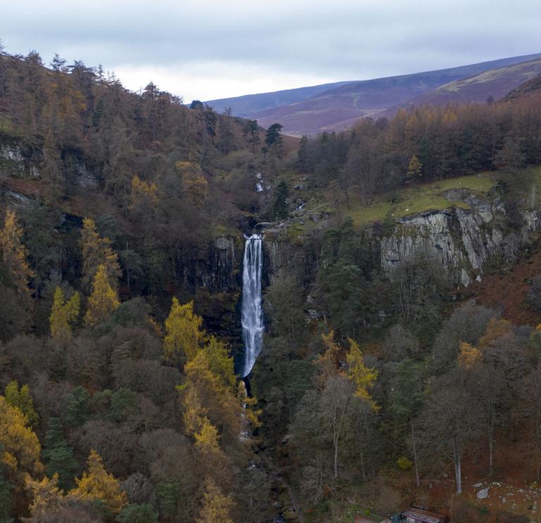 A high waterfall from above surrounded by autumn coloured trees.