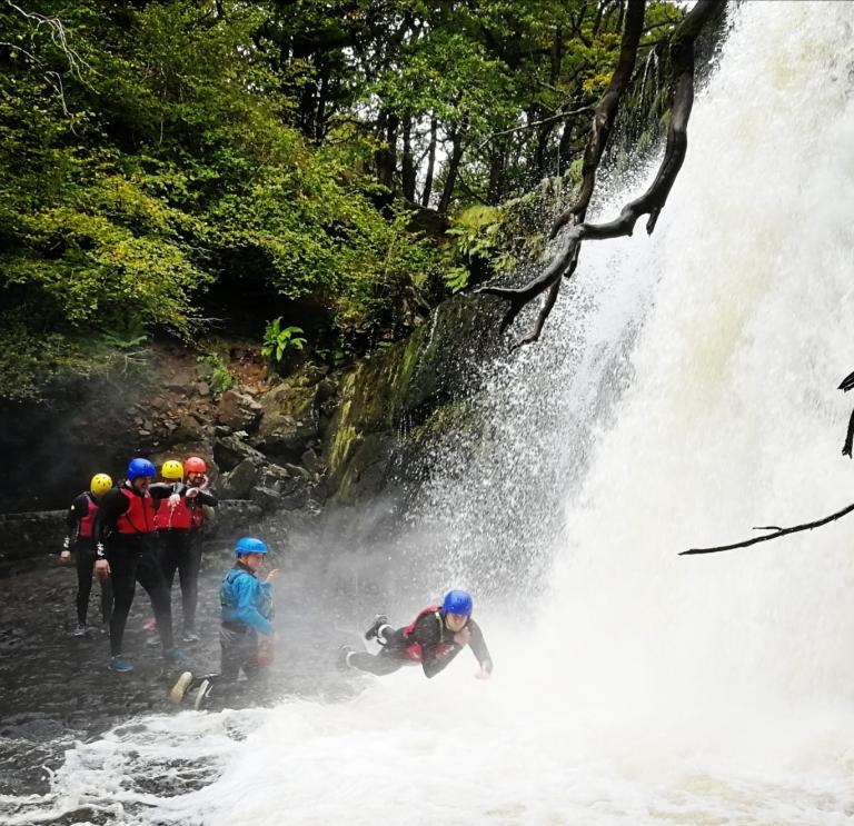 Group of adults with instructors in water, one is diving into the water with waterfall behind 