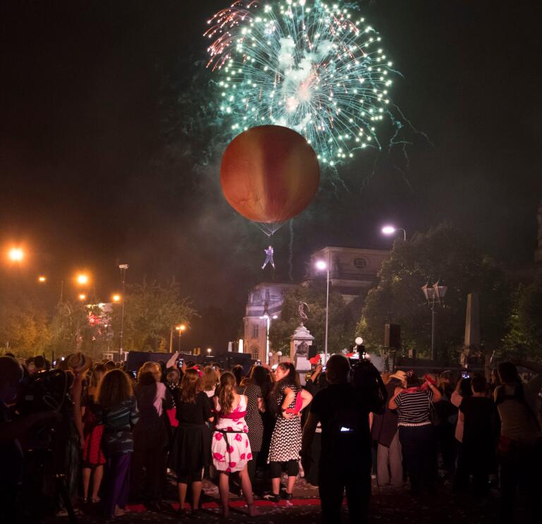 Menschenmenge beobachtet einen riesigen Pfirsich am Himmel vor einem Hintergrund von Feuerwerken