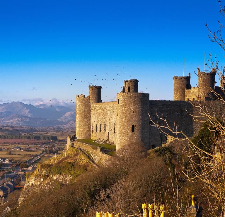 A castle on a hill surrounded by countryside with mountains in the background.