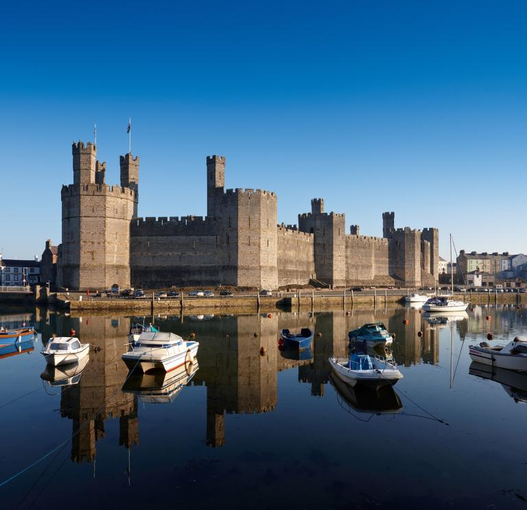 Exterior view of Caernarfon Castle from the South with boats and water.