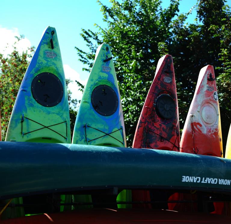 Stacked canoes by a riverside.