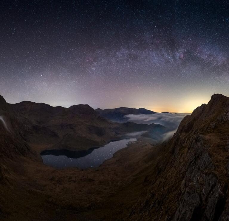 Mountain peaks in Snowdonia silhouetted against a night sky with stars and the orange glow of sunset on the horizon.