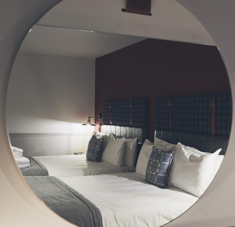 Two double beds reflected in a round mirror.