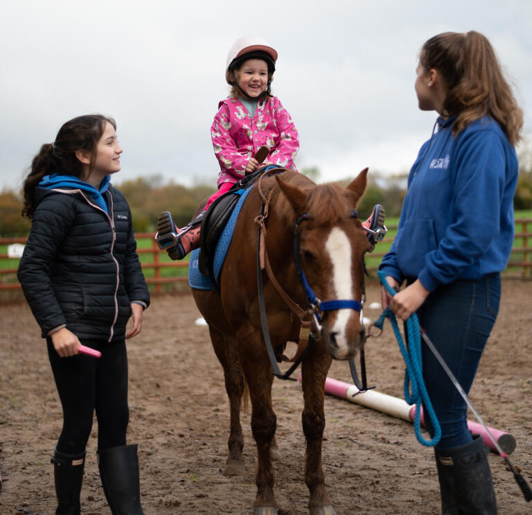 A young lady being assisted to ride a horse.