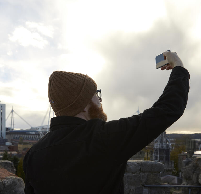 Ein Mann hält sein Handy in die Luft und macht ein Foto von Cardiff.