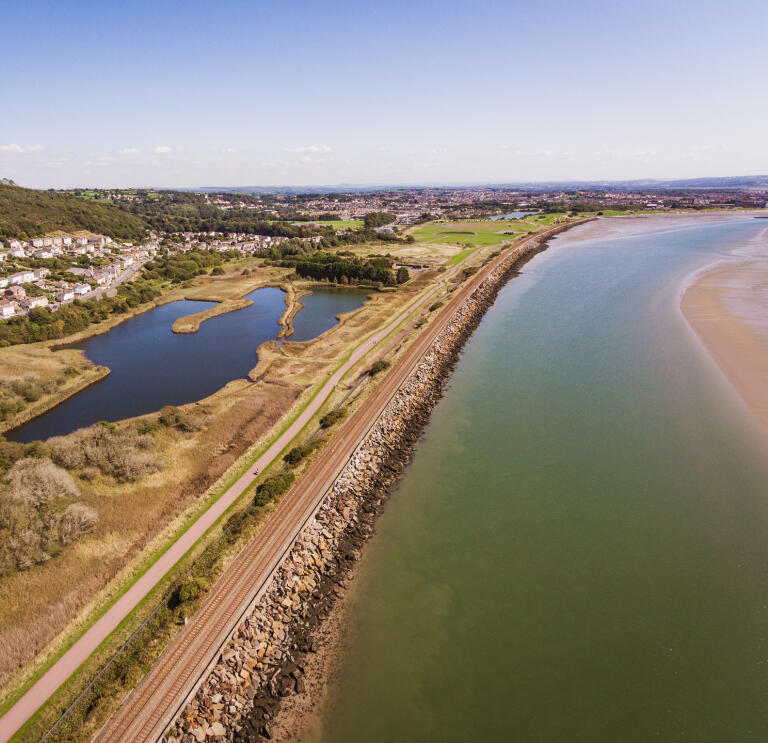 An aerial view of a coastal cycle trail passing a lake. 