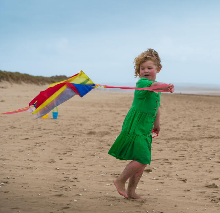 A girl flying a kite on a sandy beach.