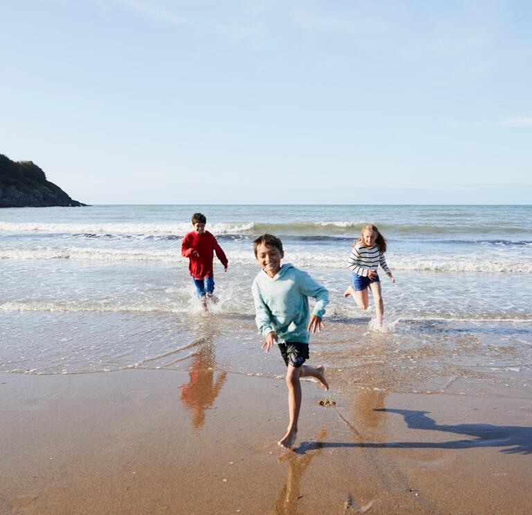 3 children running along the waters edge, playing on Aberporth Beach, Cardigan Bay, Ceredigion, West Wales