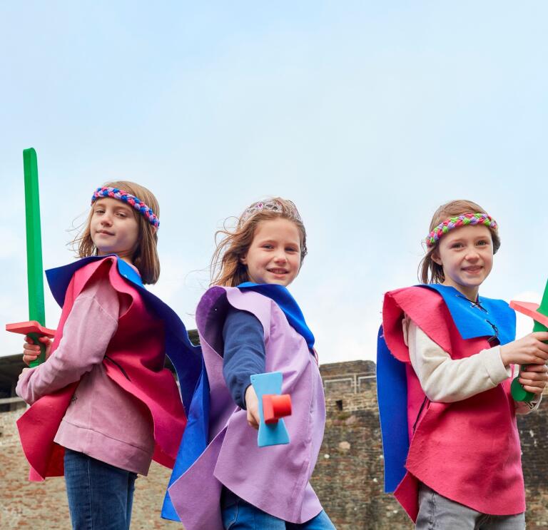 Three children dressed as knights within castle walls.