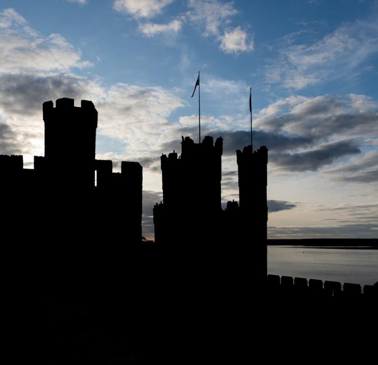 Silhouette of castle turrets and walls against a cloudy blue sky.