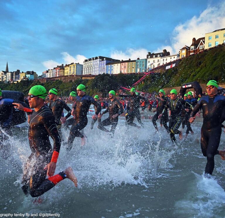 Many swimmers wearing green caps running into the sea.