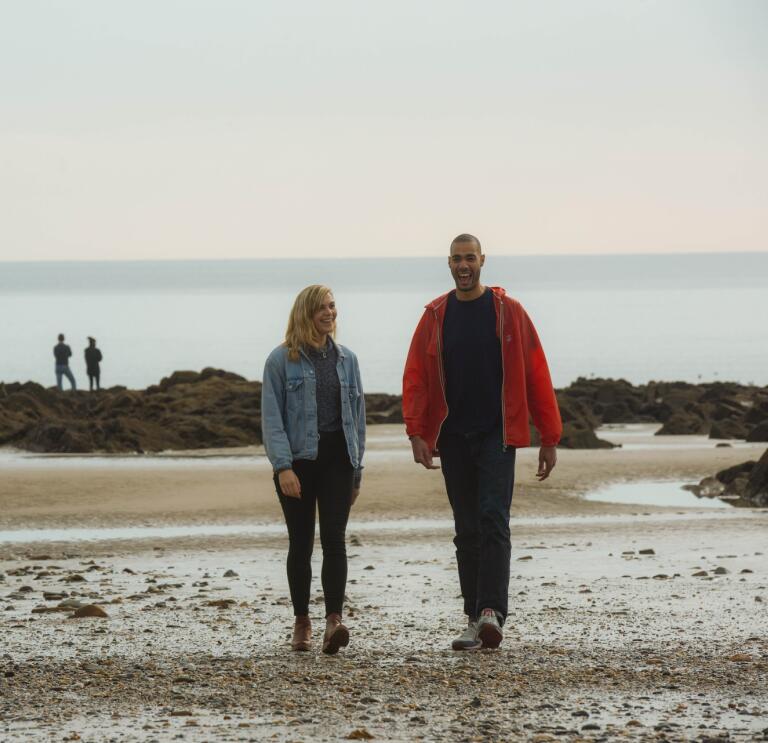 Couple walking on Saundersfoot beach with another couple standing on rocks in the distance