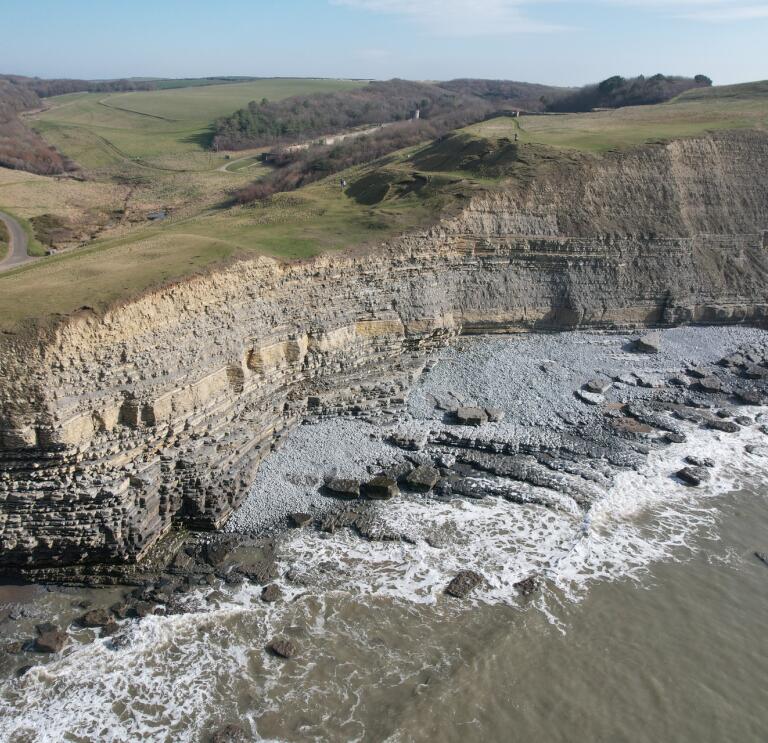 Aerial view of a limestone cliff edge over a pebbly beach.