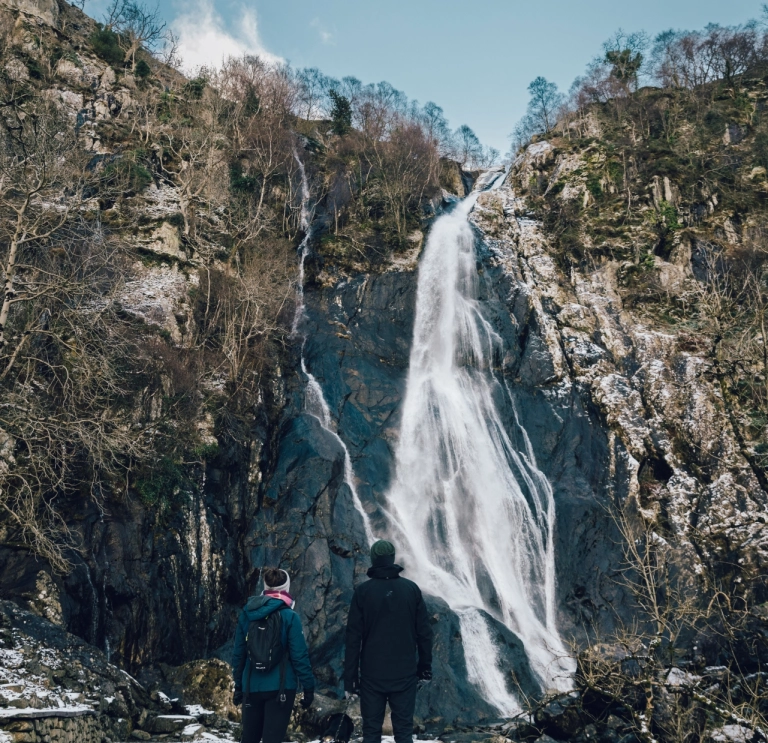 people and dogs in snow with waterfall in background.
