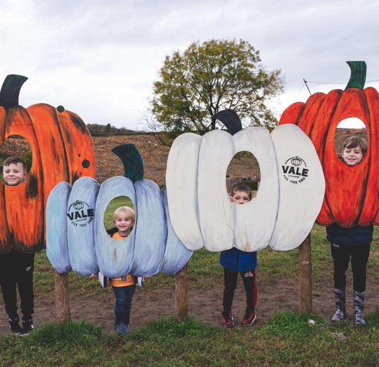 children inside pumpkin cut outs posing for photo.